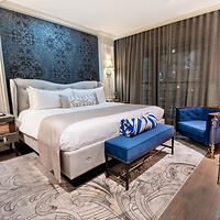 Luxurious hotel bedroom with a plush white bed, a royal blue bench at the foot, and elegant decor